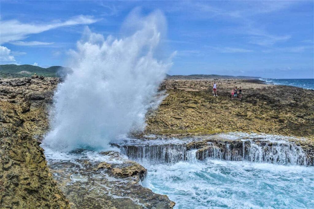 Vague d'eau qui fonce sur la falaise rocheuse et éclabousse fortement en voyage organisé sur l'île de Curaçao entre femmes #curacao #antilles #caraibes #voyageentrefemmes #voyage #voyagedegroupe #voyageorganise
